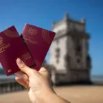 Hand holding two Portuguese passports with Belem Tower in Lisbon in the background