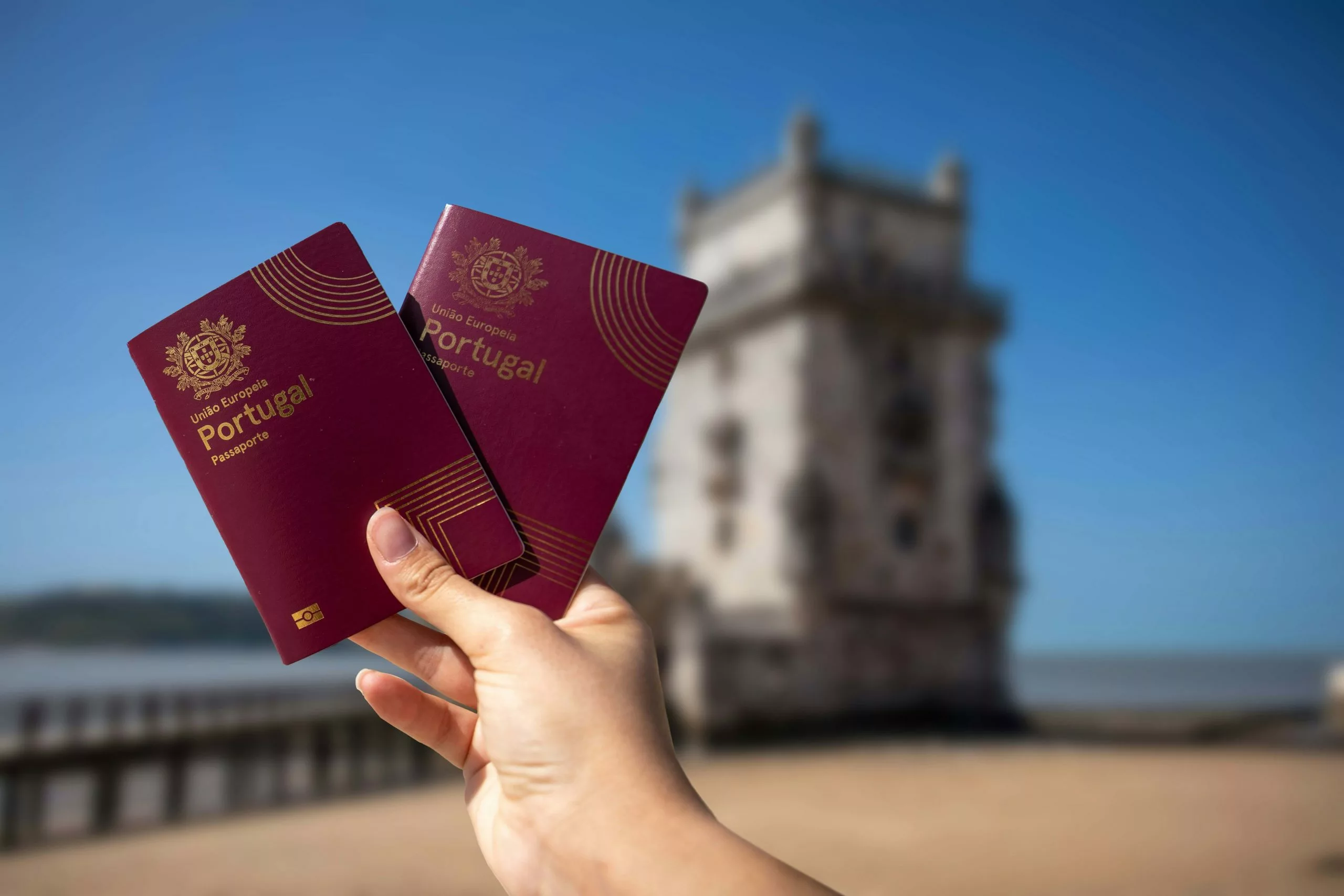 Hand holding two Portuguese passports with Belem Tower in Lisbon in the background